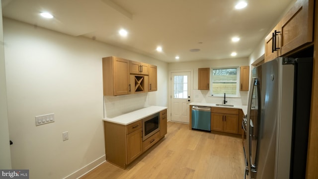 kitchen with sink, backsplash, appliances with stainless steel finishes, and light hardwood / wood-style flooring