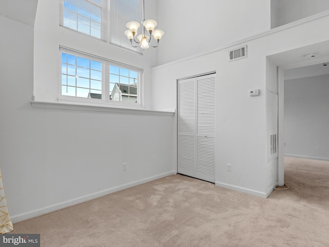 unfurnished bedroom featuring a closet, a towering ceiling, light carpet, and an inviting chandelier