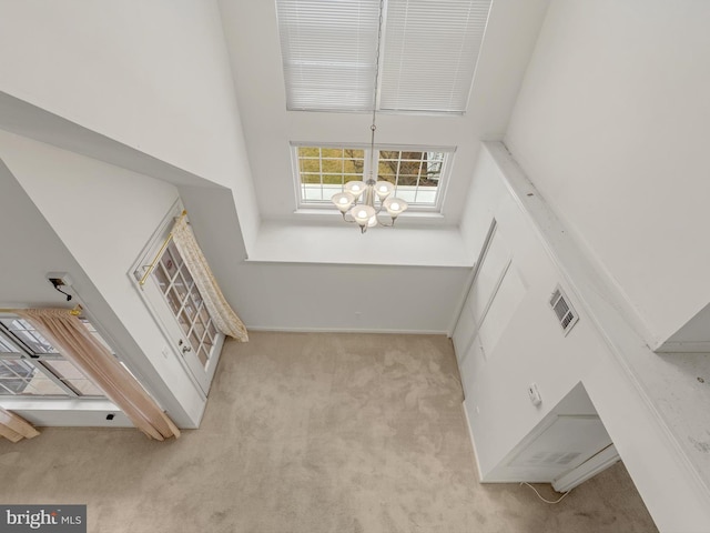 interior space featuring light carpet, a towering ceiling, and a chandelier