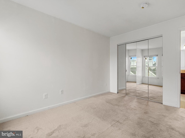 unfurnished bedroom with light colored carpet and a closet