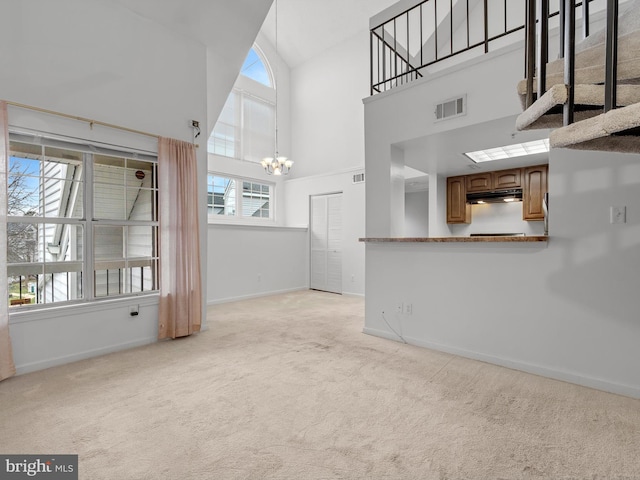 unfurnished living room featuring a healthy amount of sunlight, a chandelier, high vaulted ceiling, and light colored carpet