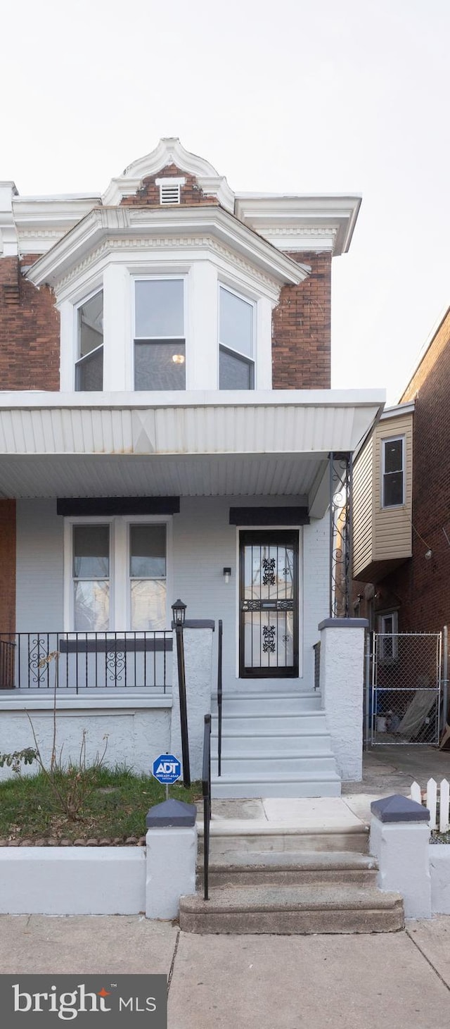 townhome / multi-family property with brick siding, covered porch, and stucco siding