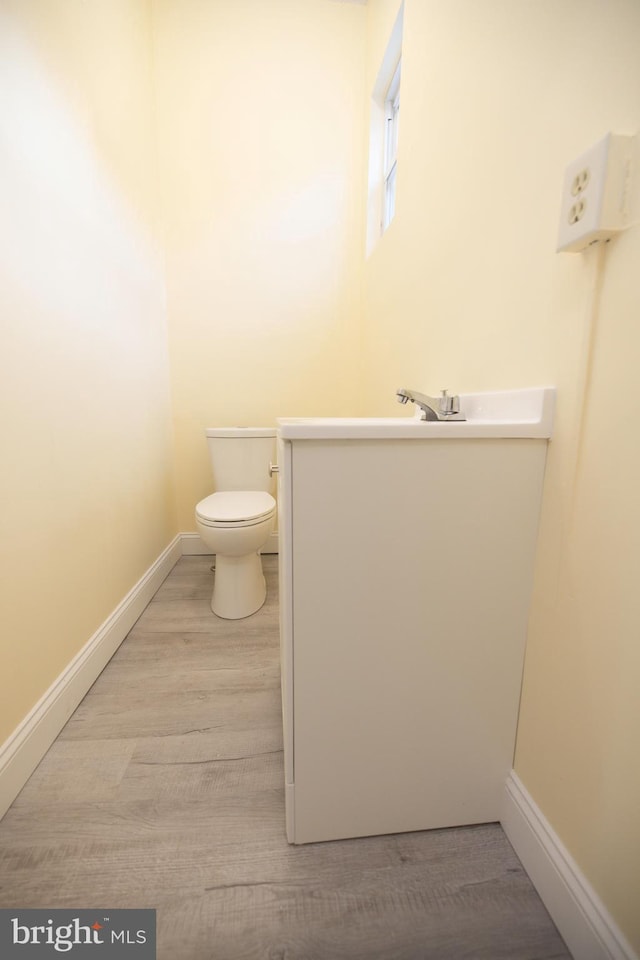 half bathroom with baseboards, toilet, wood finished floors, and vanity