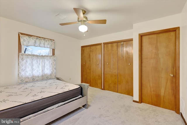 carpeted bedroom featuring ceiling fan and two closets