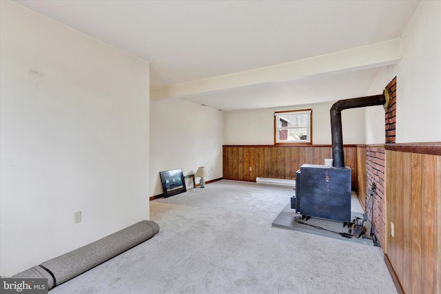 workout room featuring a wood stove, wood walls, light colored carpet, and a baseboard radiator