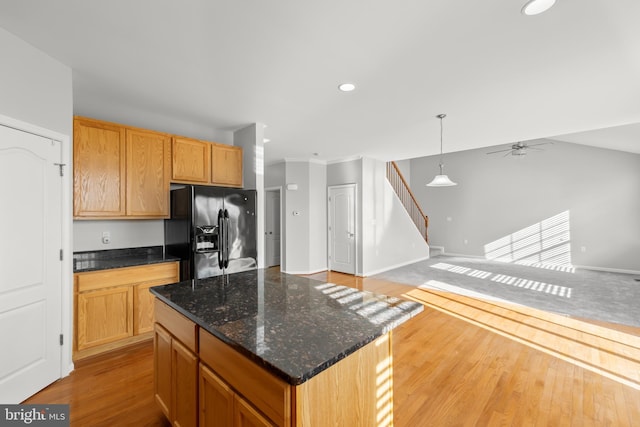 kitchen featuring black fridge with ice dispenser, ceiling fan, decorative light fixtures, dark stone countertops, and a kitchen island