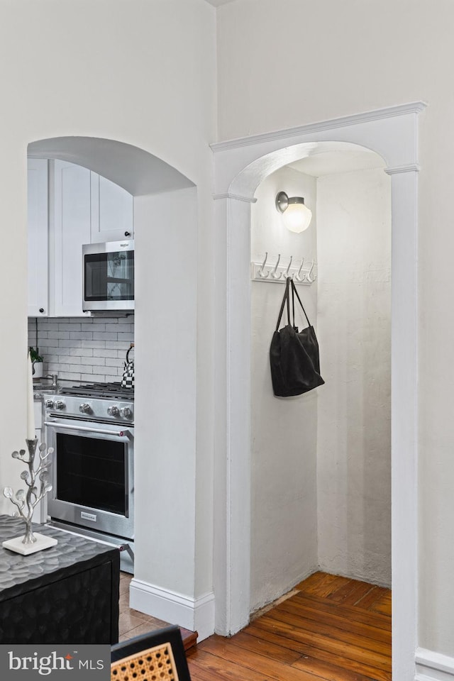 kitchen featuring tasteful backsplash, white cabinetry, stainless steel appliances, and hardwood / wood-style flooring