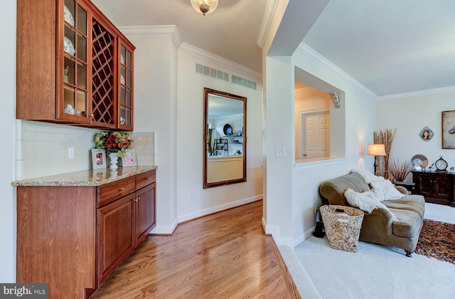 interior space featuring decorative backsplash, light stone countertops, crown molding, and light wood-type flooring