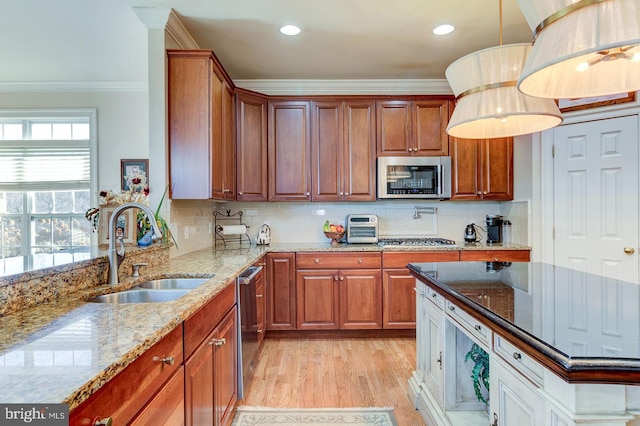 kitchen featuring appliances with stainless steel finishes, light stone counters, crown molding, sink, and hanging light fixtures