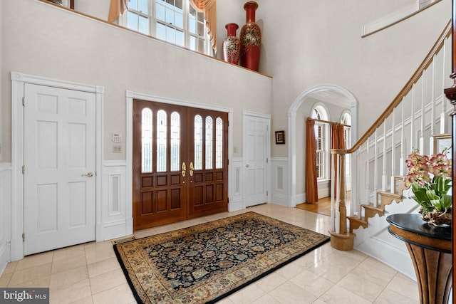 entrance foyer featuring arched walkways, wainscoting, a healthy amount of sunlight, and a decorative wall