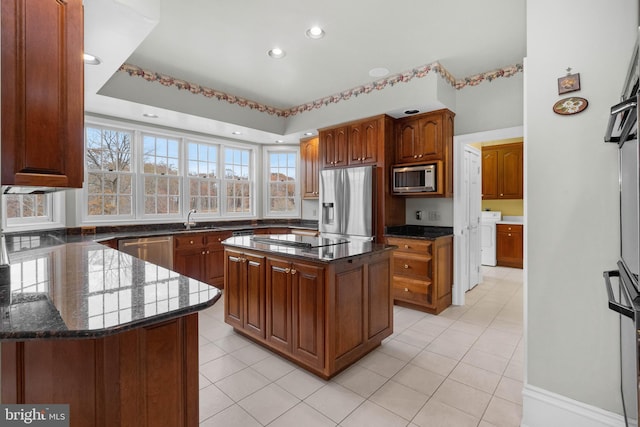 kitchen with a sink, appliances with stainless steel finishes, a center island, dark stone counters, and brown cabinetry