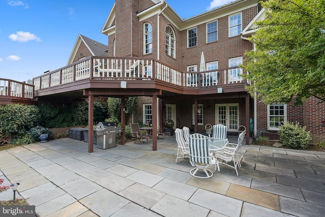 back of property featuring a patio, brick siding, outdoor dining area, and a wooden deck