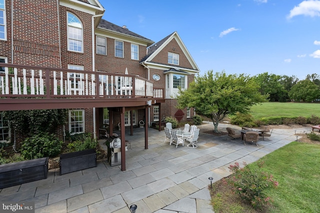 back of property featuring brick siding, a yard, a patio area, a deck, and a fire pit