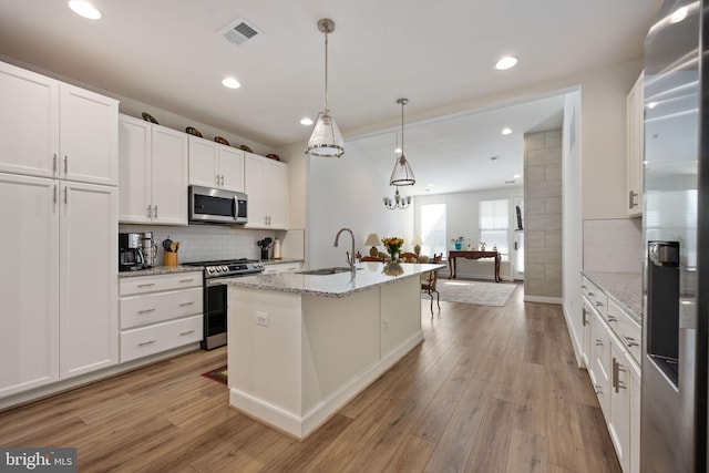 kitchen with a kitchen island with sink, sink, decorative light fixtures, white cabinetry, and stainless steel appliances