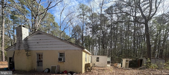 view of side of home with a chimney, concrete block siding, and cooling unit