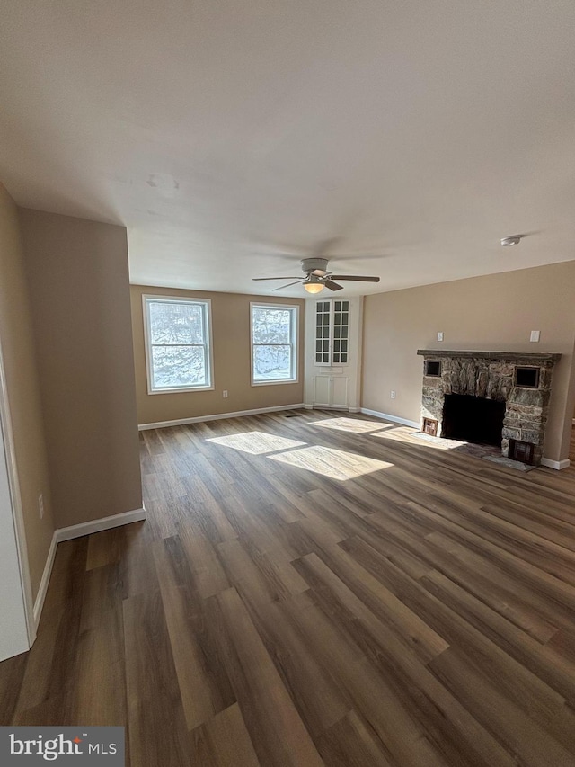 unfurnished living room with dark wood-type flooring, ceiling fan, and a stone fireplace