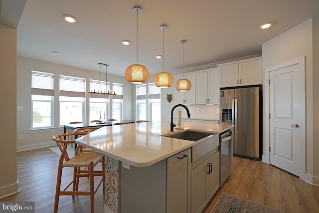 kitchen with backsplash, stainless steel appliances, sink, white cabinetry, and an island with sink