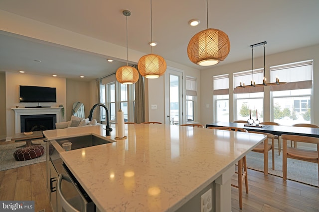 kitchen featuring light stone countertops, an island with sink, and hanging light fixtures