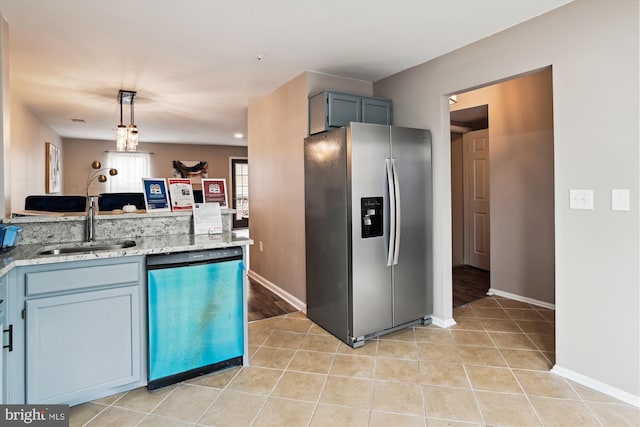 kitchen with sink, light tile patterned floors, appliances with stainless steel finishes, decorative light fixtures, and light stone counters