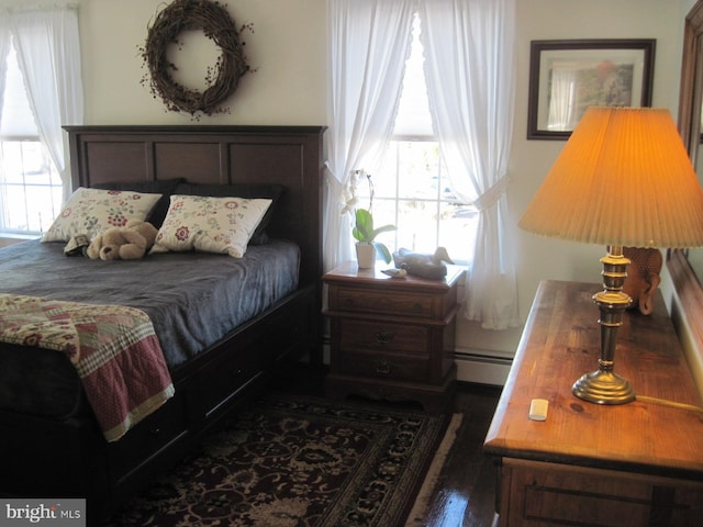 bedroom featuring dark wood-type flooring, baseboard heating, and multiple windows