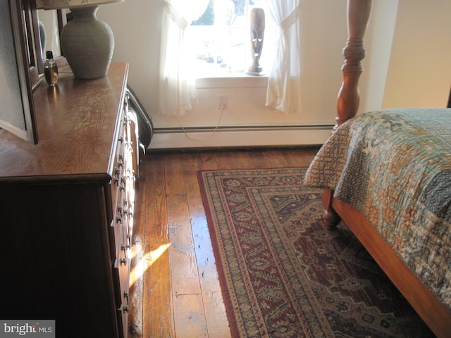 bedroom with dark hardwood / wood-style flooring and a baseboard heating unit