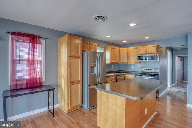 kitchen with appliances with stainless steel finishes, a kitchen island, and light hardwood / wood-style flooring