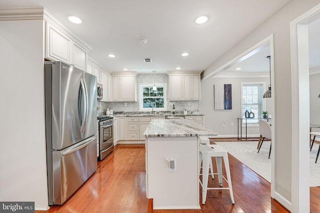 kitchen featuring white cabinetry, a center island, decorative backsplash, a breakfast bar, and appliances with stainless steel finishes