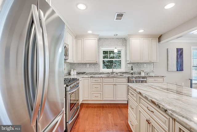 kitchen with decorative backsplash, cream cabinetry, decorative light fixtures, and appliances with stainless steel finishes