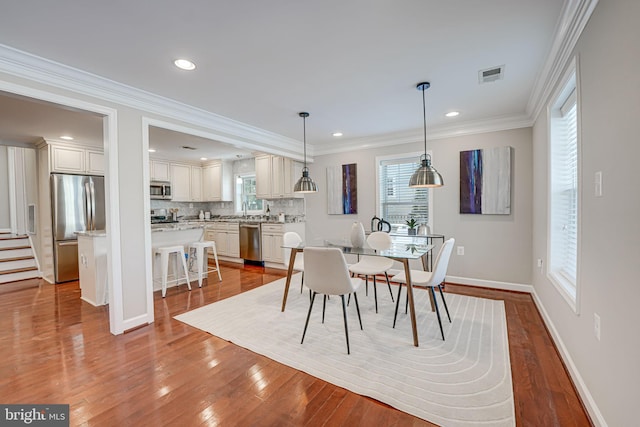 dining area with crown molding, sink, and light wood-type flooring