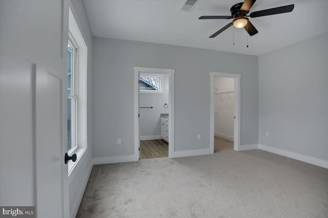 unfurnished bedroom with ceiling fan, multiple windows, a walk in closet, light carpet, and a closet