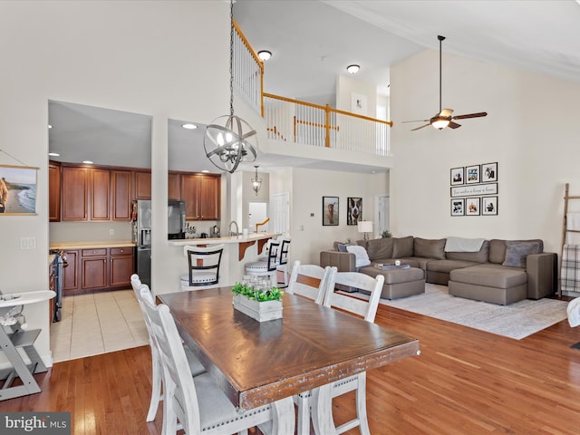 dining area featuring a towering ceiling, light hardwood / wood-style floors, and ceiling fan with notable chandelier