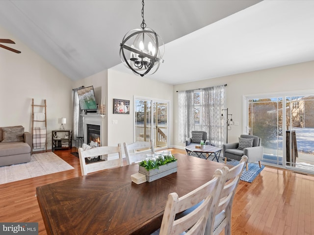 dining room featuring ceiling fan with notable chandelier, light wood-type flooring, and vaulted ceiling