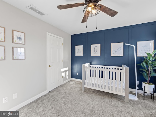 bedroom featuring ceiling fan, a nursery area, and light carpet