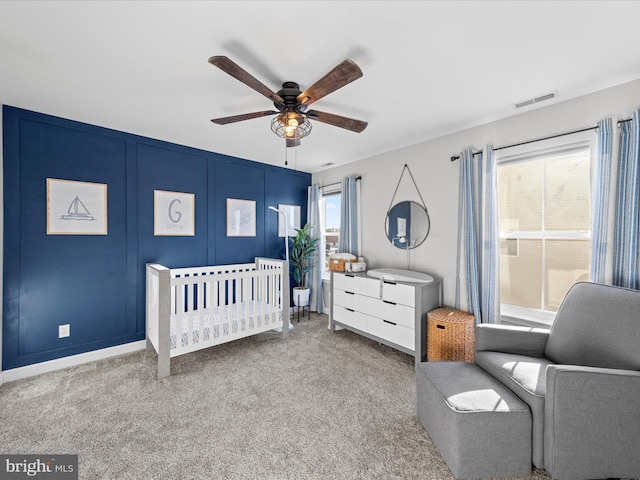 carpeted bedroom featuring multiple windows, ceiling fan, and a nursery area