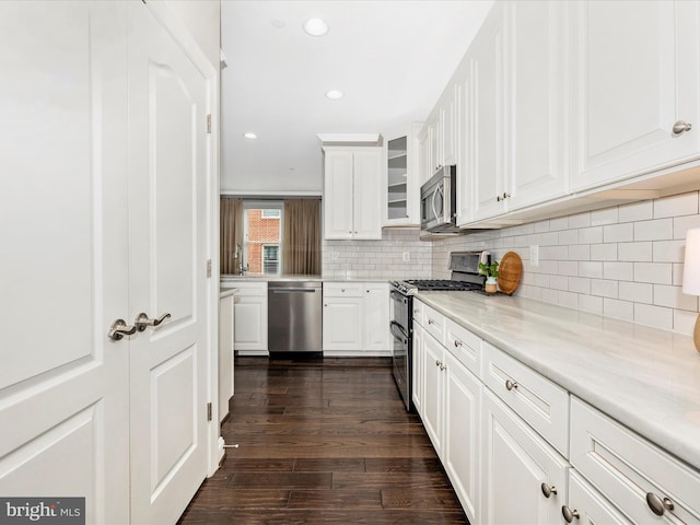 kitchen with white cabinetry, stainless steel appliances, decorative backsplash, dark hardwood / wood-style floors, and light stone counters