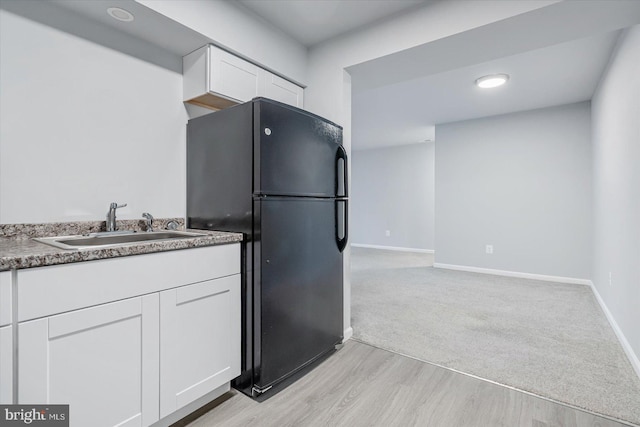 kitchen featuring black refrigerator, white cabinets, light hardwood / wood-style flooring, and sink