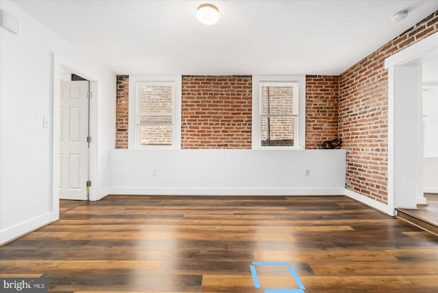 empty room with dark hardwood / wood-style flooring and brick wall