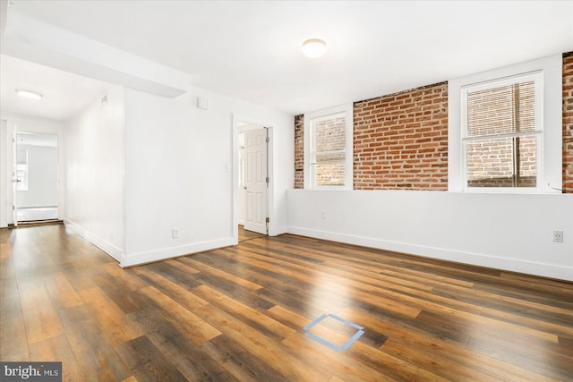 empty room featuring dark hardwood / wood-style floors, a baseboard heating unit, and brick wall