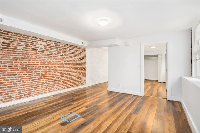 empty room with dark hardwood / wood-style flooring and brick wall