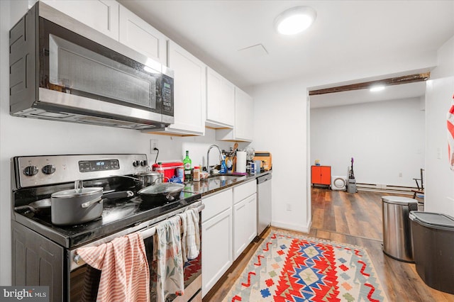 kitchen featuring sink, a baseboard radiator, wood-type flooring, white cabinets, and appliances with stainless steel finishes