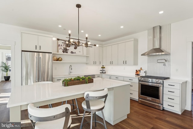 kitchen featuring wall chimney range hood, high quality appliances, a kitchen bar, decorative backsplash, and white cabinets