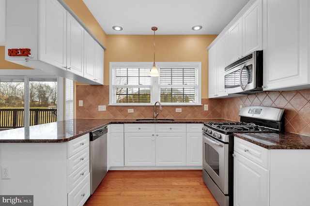 kitchen with kitchen peninsula, appliances with stainless steel finishes, sink, white cabinets, and hanging light fixtures