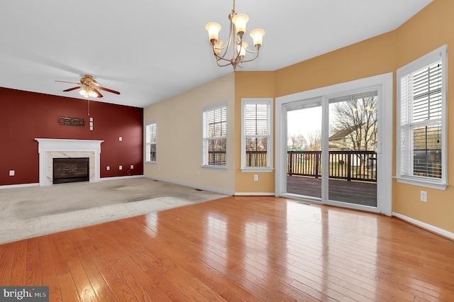 unfurnished living room featuring ceiling fan with notable chandelier, a high end fireplace, and light hardwood / wood-style flooring