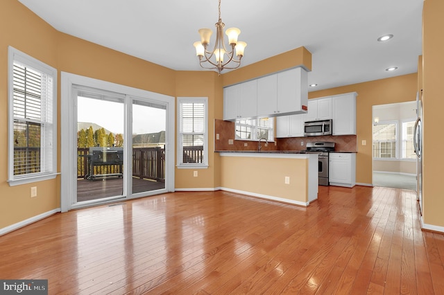 kitchen featuring white cabinets, decorative light fixtures, kitchen peninsula, stainless steel appliances, and a chandelier