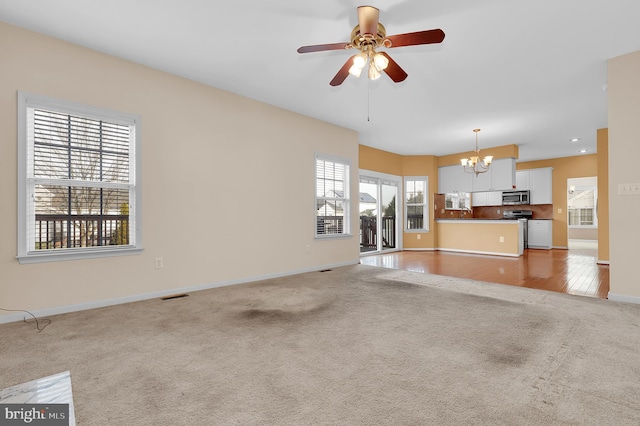 unfurnished living room with ceiling fan with notable chandelier and light colored carpet