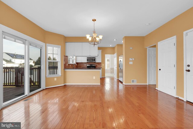 kitchen with kitchen peninsula, appliances with stainless steel finishes, a chandelier, white cabinetry, and hanging light fixtures