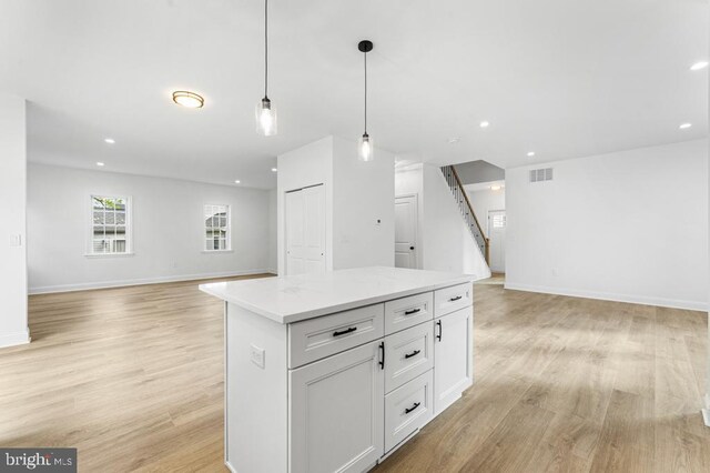 kitchen with white cabinets, a kitchen island, hanging light fixtures, and light wood-type flooring