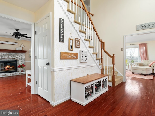 staircase featuring ceiling fan, hardwood / wood-style floors, and a brick fireplace