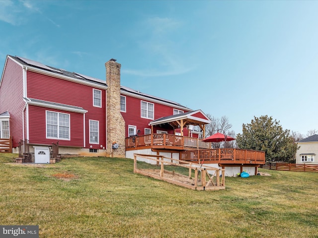 rear view of property featuring a lawn, solar panels, and a wooden deck