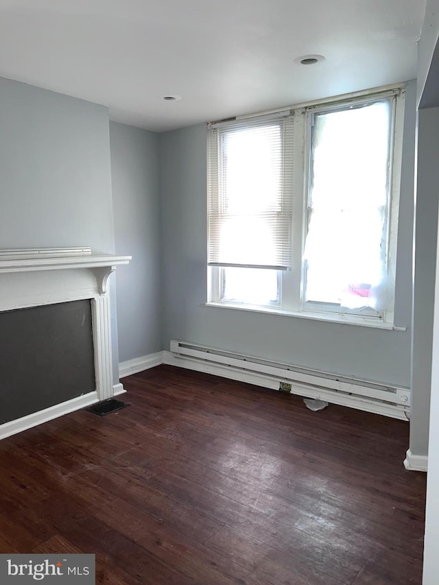 unfurnished living room featuring dark wood-type flooring and a baseboard heating unit